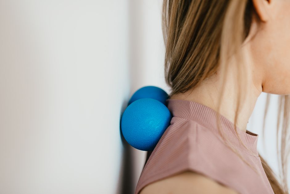 Side view crop unrecognizable female leaning on small balls against wall to massage stiff neck muscles and sore neck